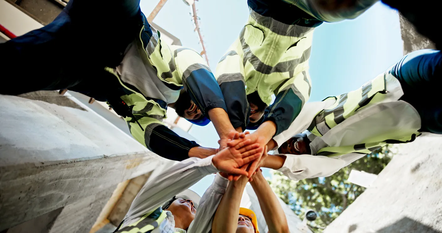 A crew in hi-vis gear stacking hands in a huddle, seen from below